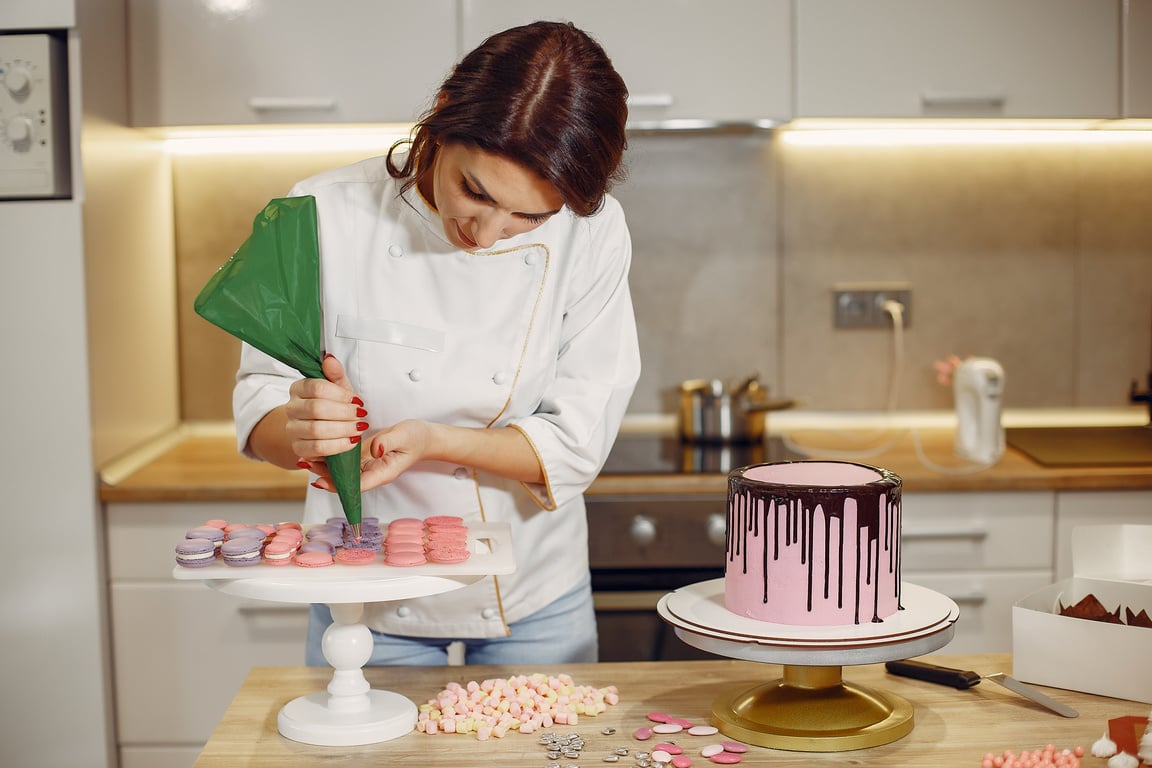 Female pastry chef adding cream on macaroons shells in modern bakery